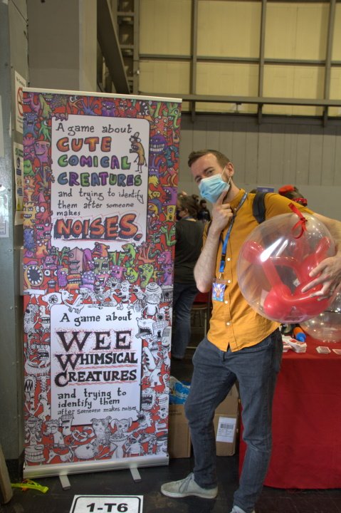 The Uk games expo non awards awards stuff by bez - a picture of a man in an orange shirt holding a balloon and looking puzzled next to a poster for a game about cute comical creatures