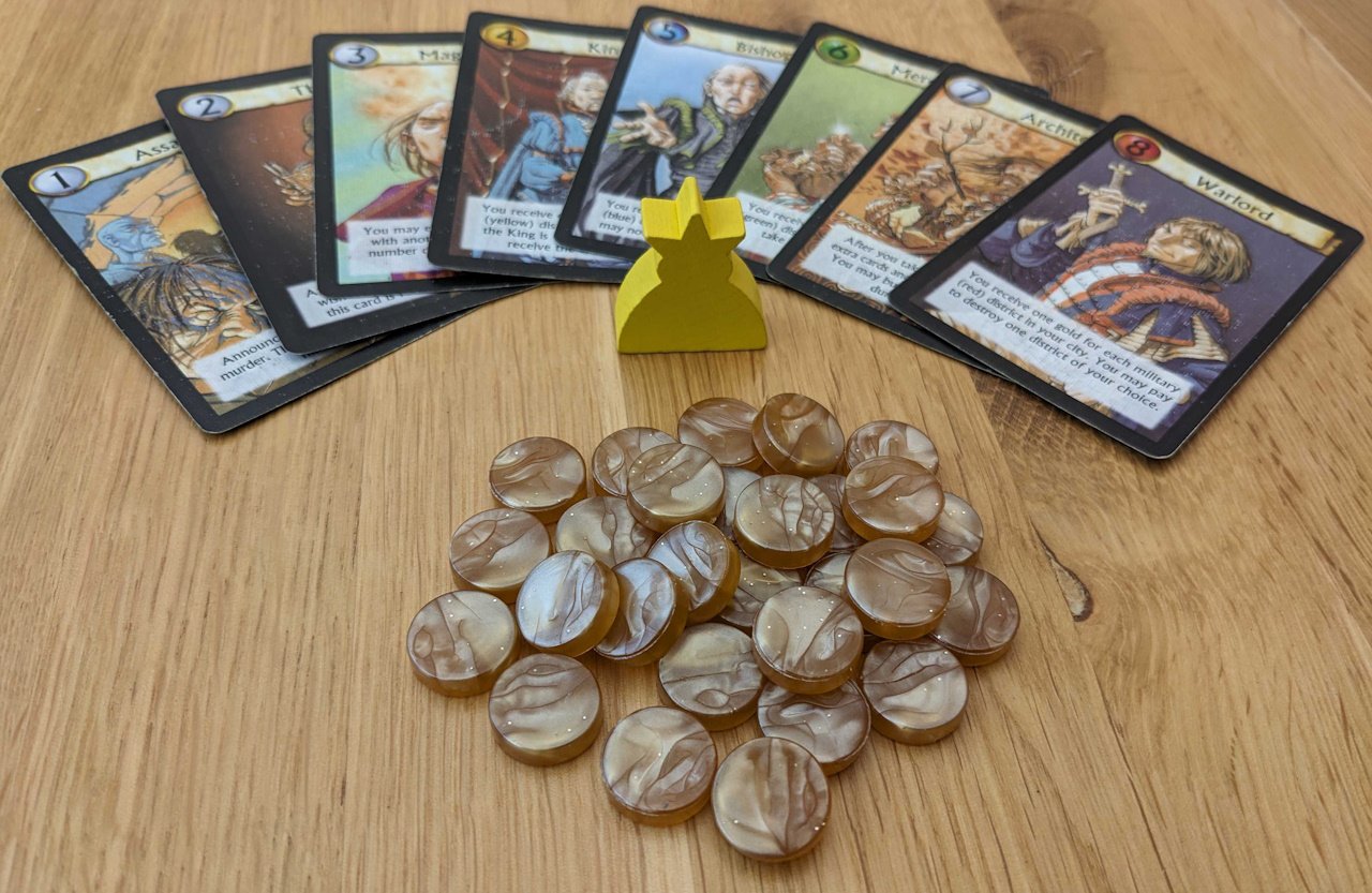 temptingly tasty board game components citadels - the character cards are splayed in an ark above the king token and the gold tokens