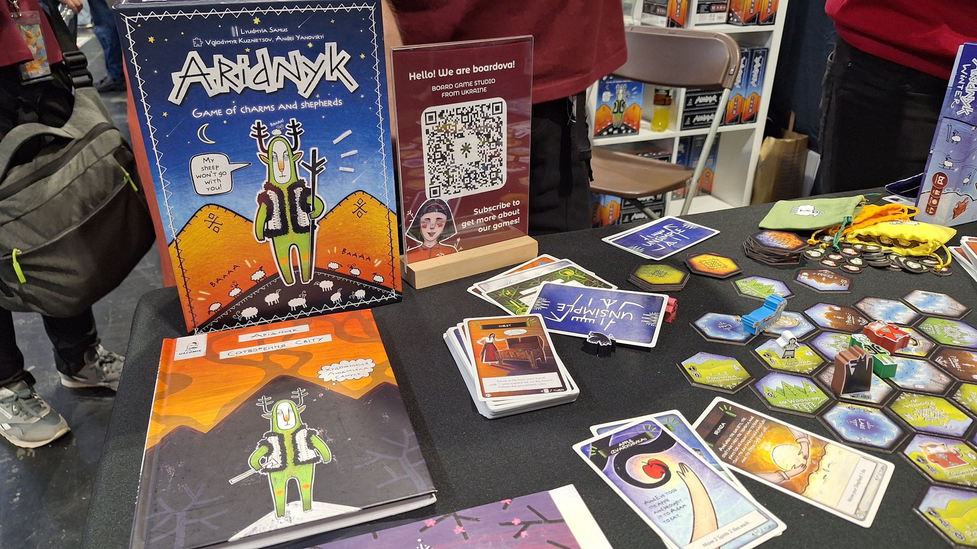 Ukrainian board game aridnyk at UKGE 2026 - a sigure with a staff stands on the box cover in front of the game pieces and card lain out below