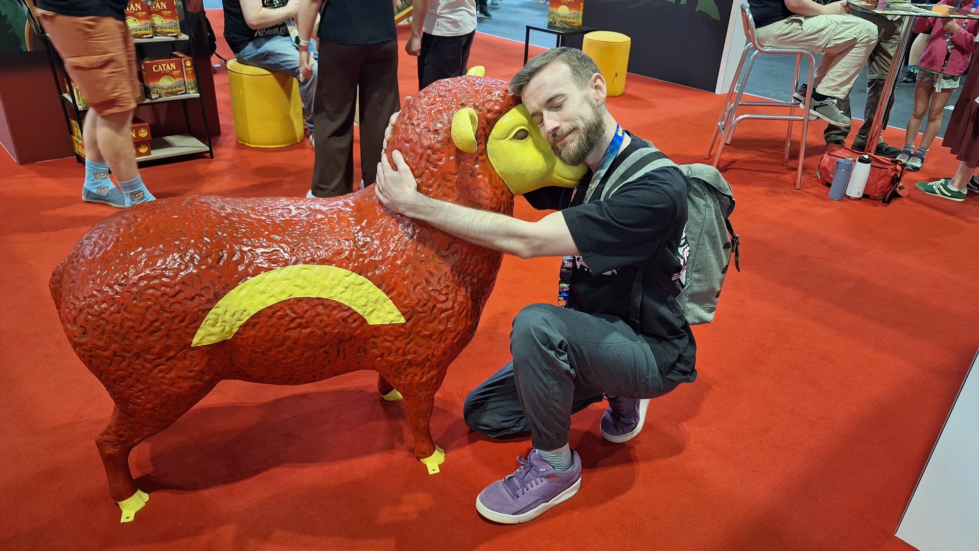 Me kneelingg down to hug the Catan sheep statue at UKGE 2026